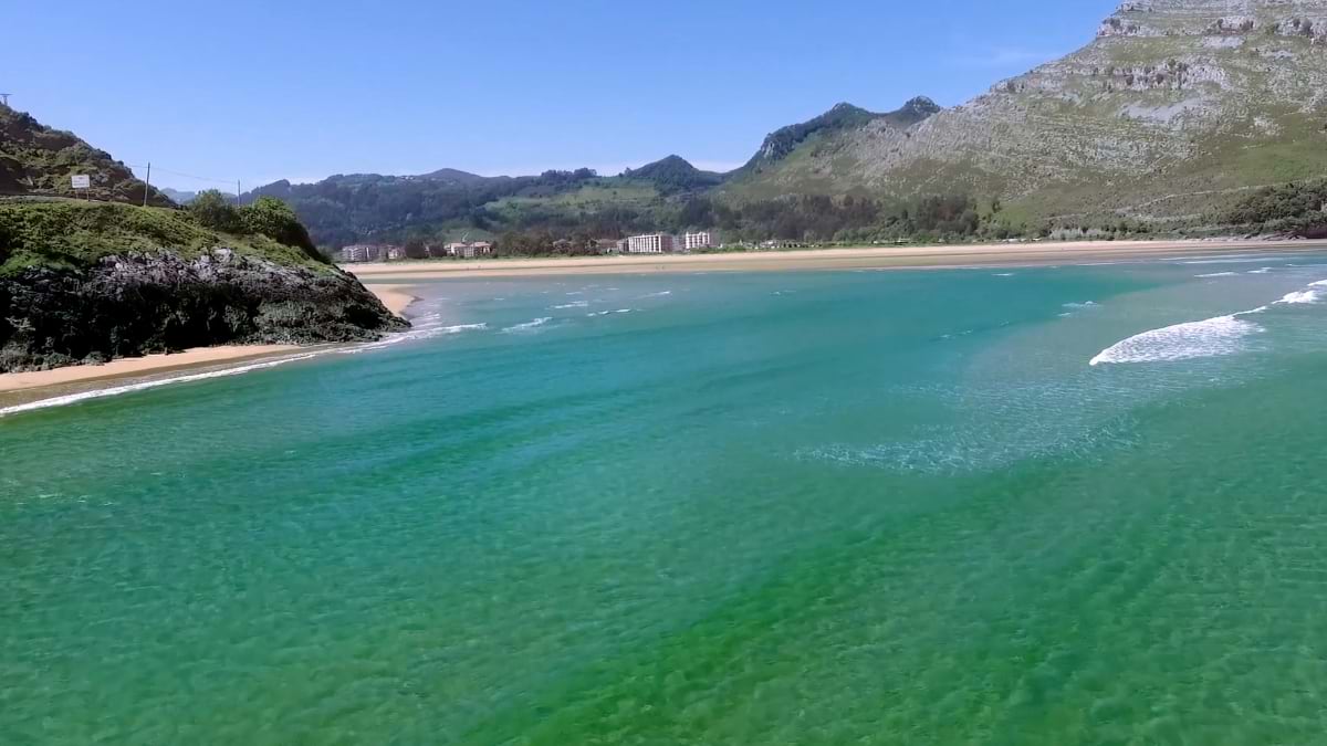 Turquoise waters and sandy beach in Cantabria, framed by green mountains and rocky outcrops along the northern Spanish coast