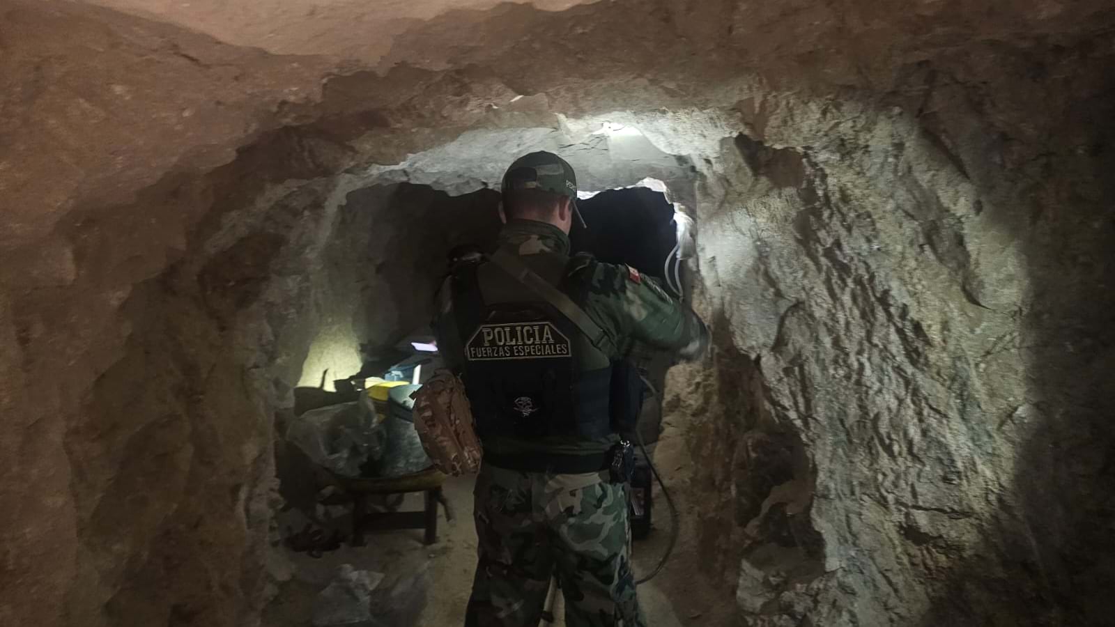 Police officers with tactical patches crawling through narrow underground tunnel illuminated by flashlights during investigation.