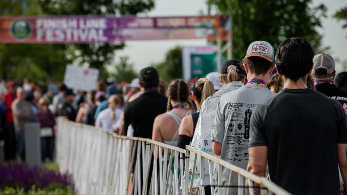 Marathon runners and spectators behind metal barriers at Oklahoma City Memorial Marathon with festival banners visible in background.