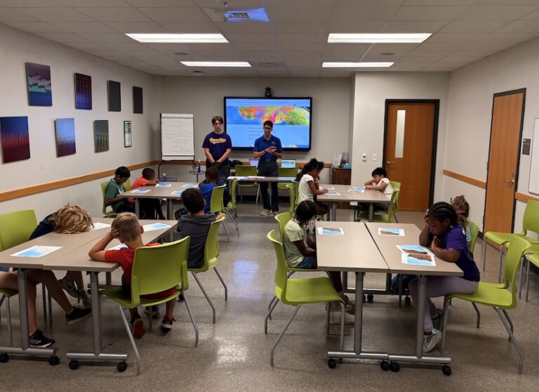 A classroom with students sitting at tables watching a presentation