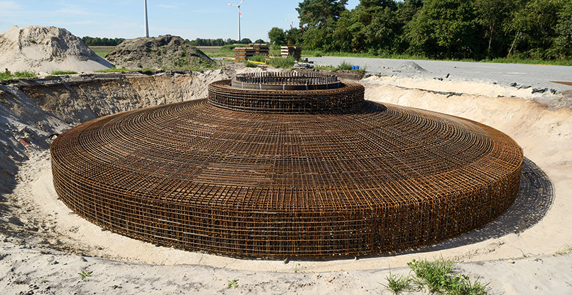 A large, circular rebar foundation sits in a sandy pit for a wind turbine.