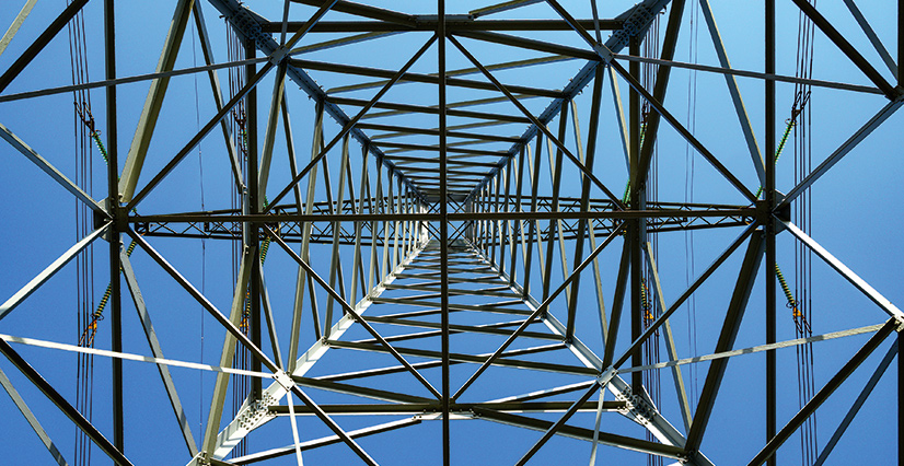A worm's-eye view of a metal electrical tower against a clear blue sky.