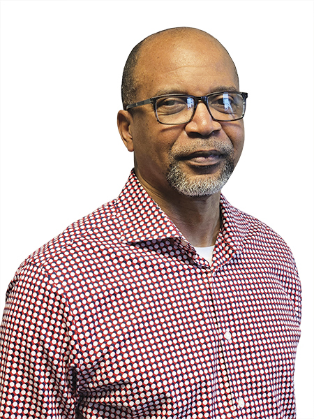 A man wearing glasses and a red checkered collared shirt standing, facing the camera, smiling pleasantly.