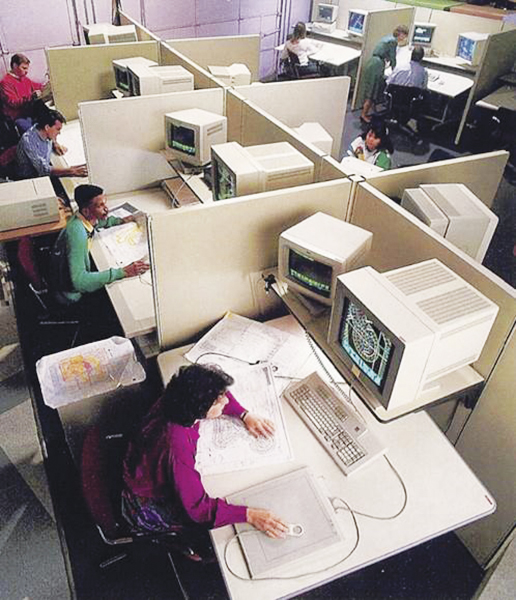 An aerial view of an office with cubicles and people working on computers with large monitors.
