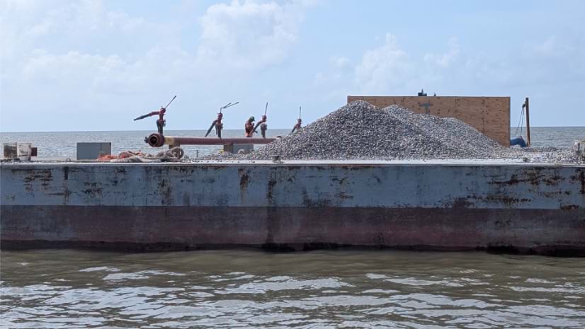 Aerial view of barges loaded with oyster shells alongside work barge with excavator in Louisiana waters