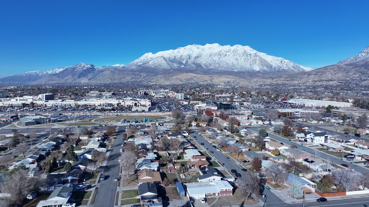 Aerial view of Orem, Utah with residential streets and commercial areas bounded by snow-covered mountain ranges.