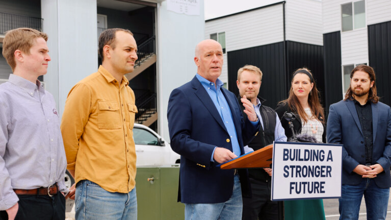 Governor Gianforte speaks at outdoor podium with "Building a Stronger Future" sign, flanked by six people at Montana housing reform announcement.