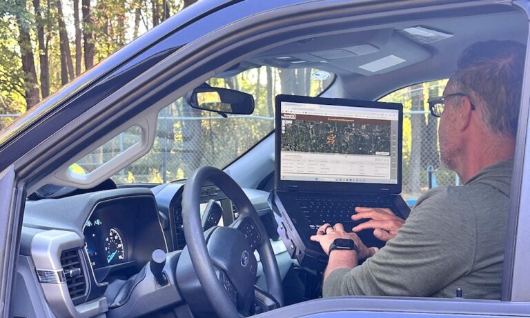 A man in a vehicle typing on a laptop