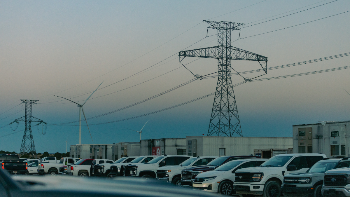 Parking lot filled with white work trucks at SunZia construction site, with transmission towers and wind turbines visible in background