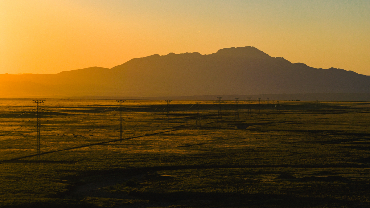 Transmission towers silhouetted against golden sunset sky stretching across desert landscape with mountains in background in New Mexico