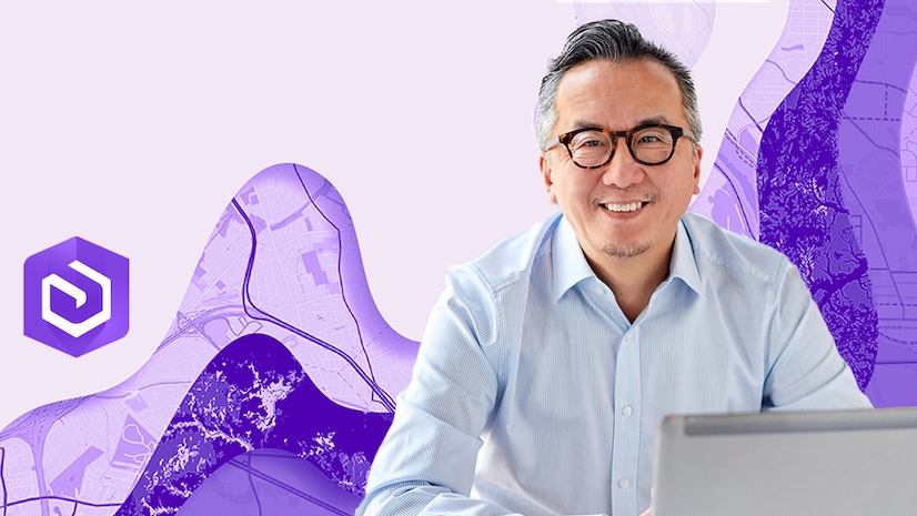 A smiling professional man working on a laptop against a purple background
