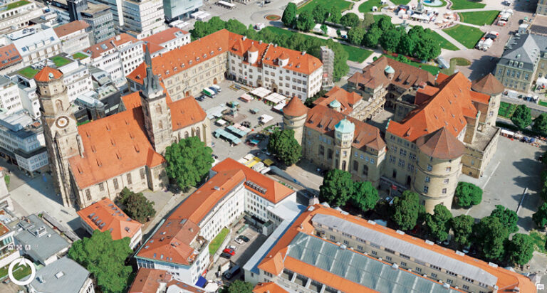 An aerial view in a digital twin of a historic European city center with a stone church, a clock tower, and a red-tiled castle complex around a market square.