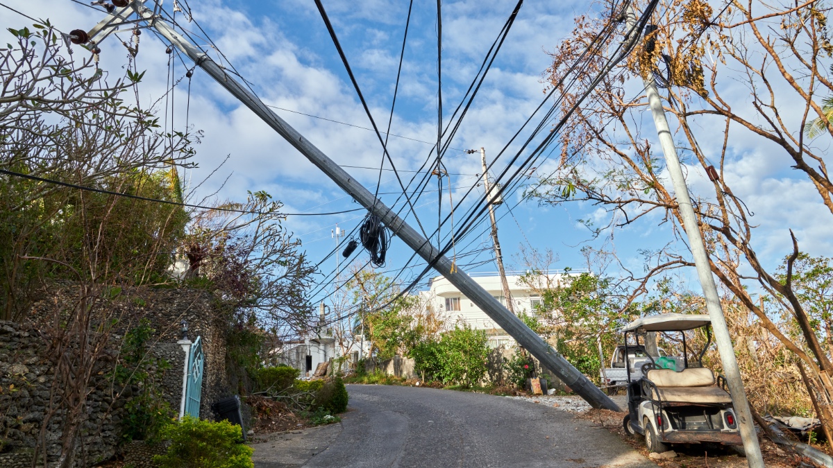 Leaning utility pole with tangled power lines on Boracay Island street after Typhoon Ursula, with damaged trees and abandoned vehicle visible.