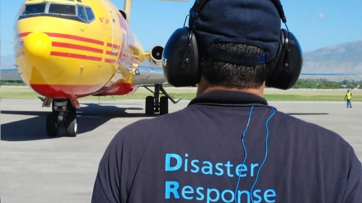 Disaster response worker in headphones facing yellow cargo aircraft on tarmac, preparing for typhoon relief mission in the Philippines.
