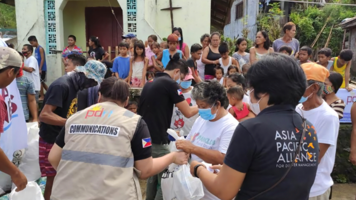 Relief workers from PLDT Communications and Asia Pacific Alliance distributing aid packages to crowd of families and children after Typhoon Goni.