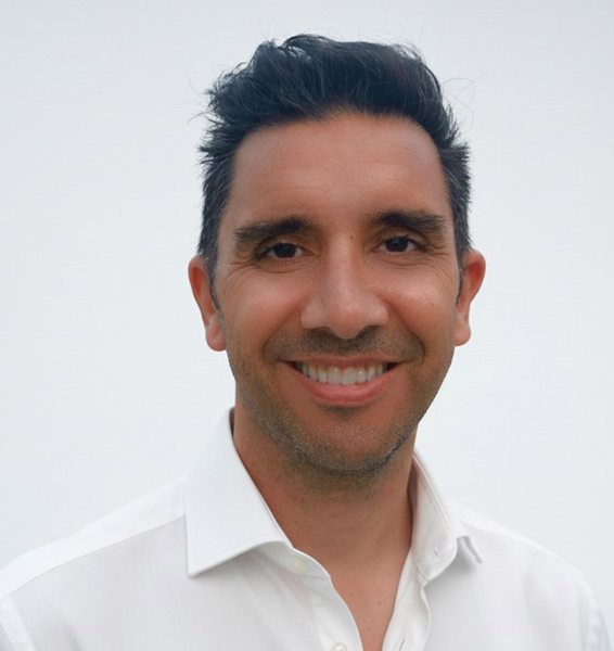 A headshot of a smiling man with dark hair, wearing a white collared shirt against a light background.