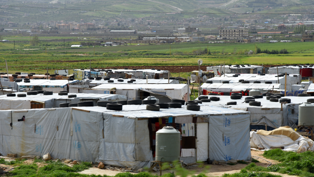 Makeshift shelters with UNHCR tarps and tire-weighted roofs in Syrian refugee camp, Bekaa Valley, Lebanon