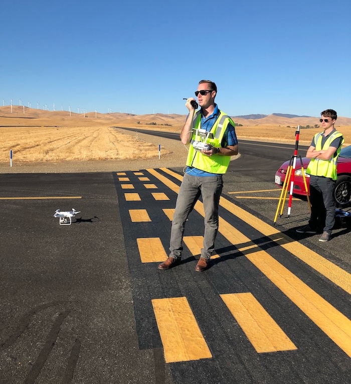 A drone pilot in a yellow safety vest on a runway with a drone
