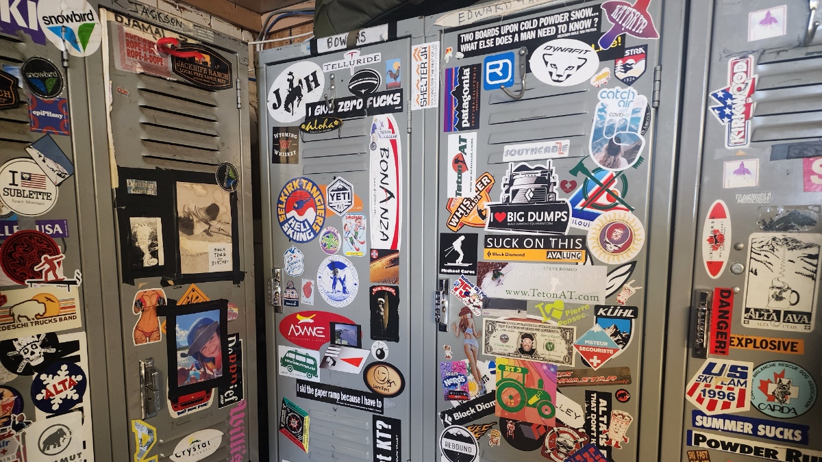 Metal ski patrol lockers densely covered with vintage and modern stickers including ski resort logos, brand names, and humorous phrases.
