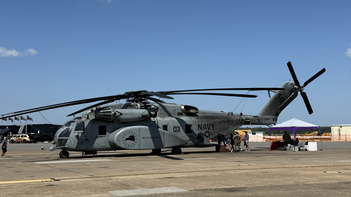 Navy CH-53 Sea Stallion helicopter on display at air show with visitors and vendor tents in background.
