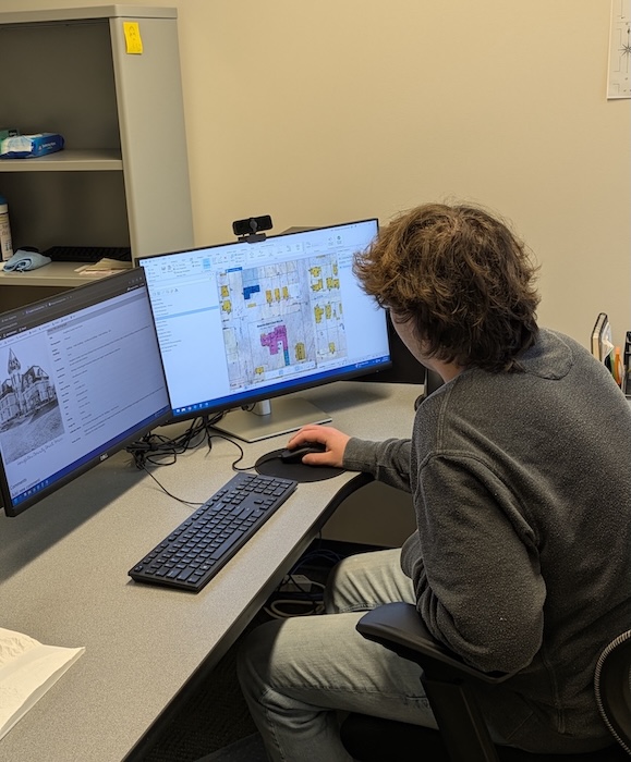 A young student working on a computer with two monitors