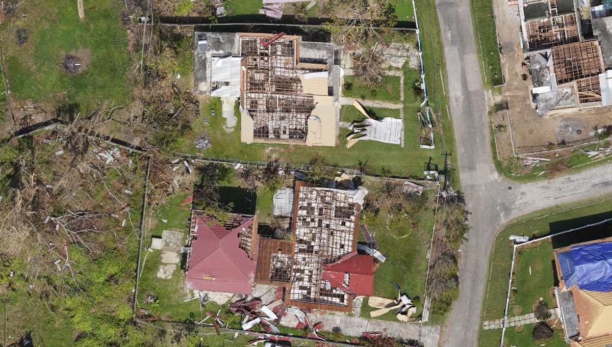 Aerial view of a Jamaican neighborhood with multiple homes stripped to bare roof rafters by Hurricane Melissa.