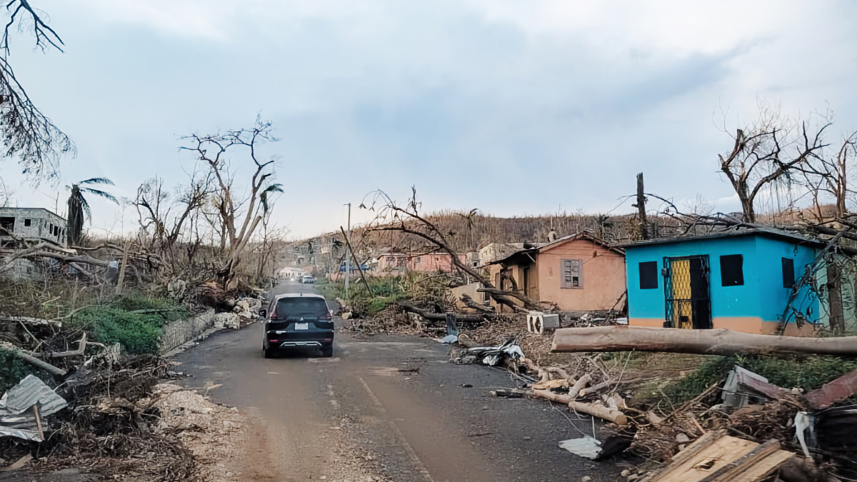 A car navigates debris-covered streets in western Jamaica lined with fallen trees and storm-damaged homes after Hurricane Melissa.