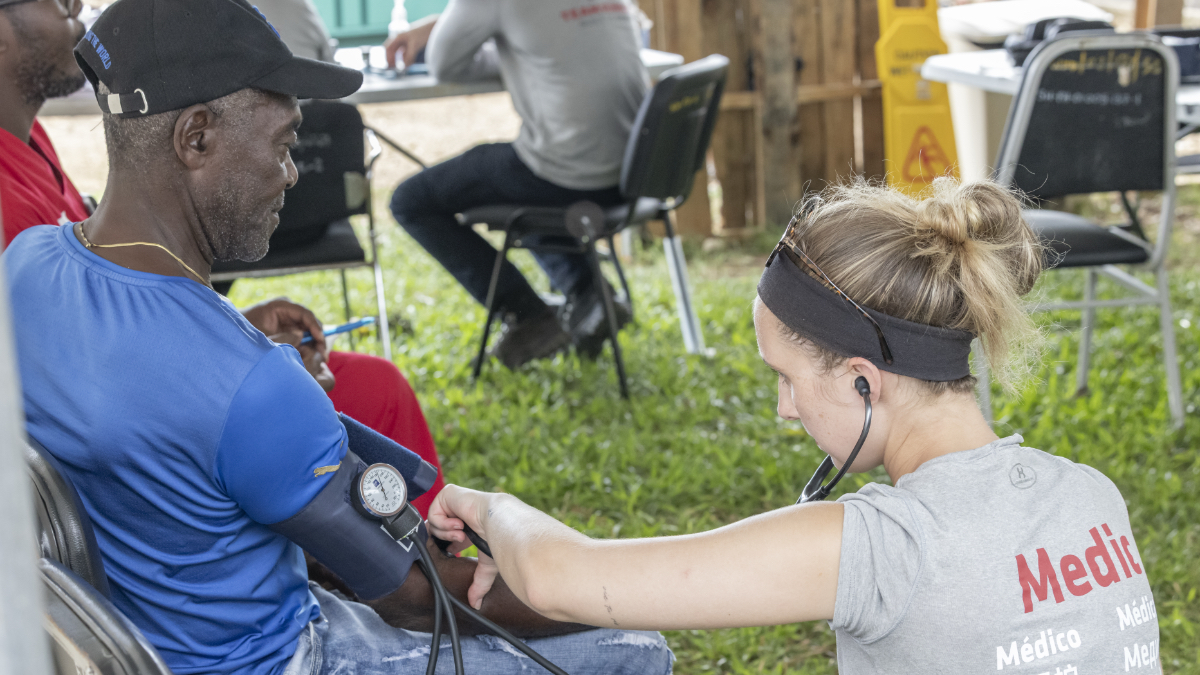 A Team Rubicon medic takes a patient's blood pressure at an outdoor field clinic in Jamaica following Hurricane Melissa.
