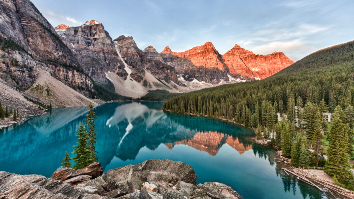 Moraine Lake in Banff National Park, with glacier-carved peaks reflected in turquoise water at sunrise, surrounded by evergreen forest.