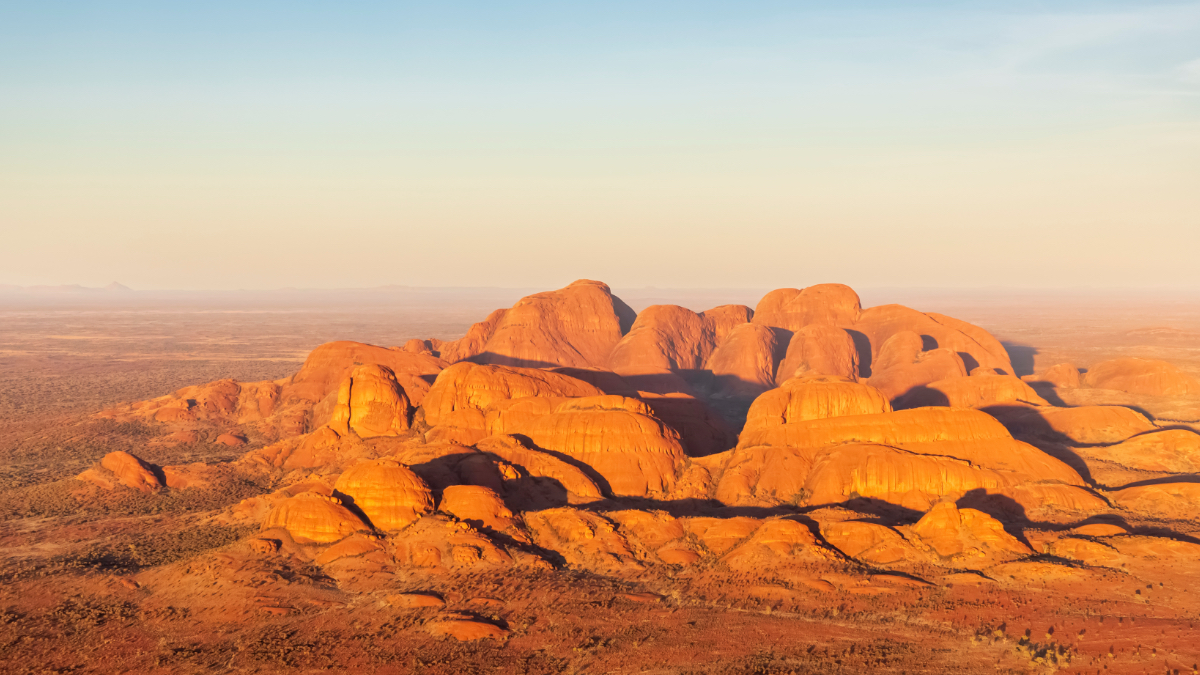 Aerial view of Kata Tjuta's domed red rock formations glowing in warm desert light, Northern Territory, Australia.