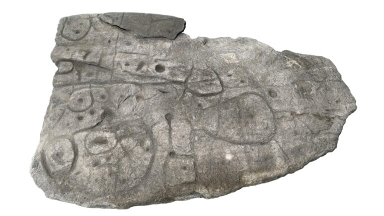 Top view of the dalle de Saint-Bélec, a flat grey schist slab engraved with circular forms, cupules, and sinuous lines mapping Bronze Age Brittany.