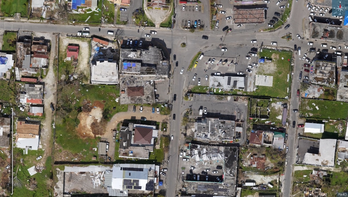 Overhead drone orthomosaic of a town intersection showing storm-damaged rooftops, blue tarps, and debris after Hurricane Melissa.