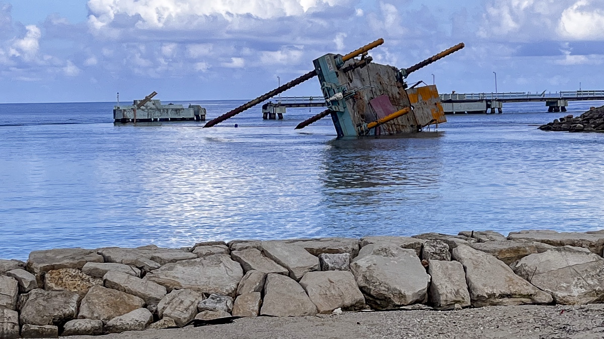 Collapsed dock structure partially submerged in a Jamaican harbor with broken concrete and exposed rebar after Hurricane Melissa.