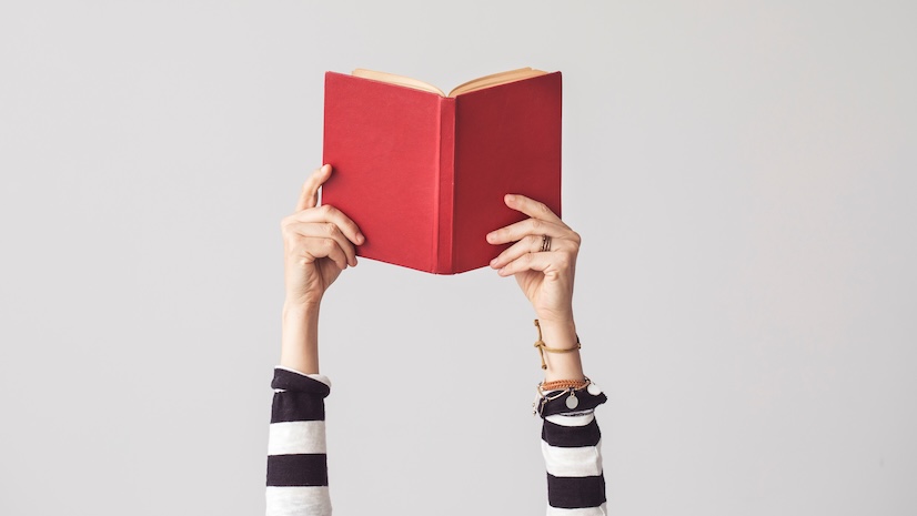 A set of hands holding an open red book