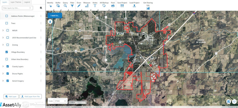 A screenshot of GIS software showing an aerial map of Mukwonago, Wisconsin, with the village boundary outlined in red. A layers panel on the left lists data options.