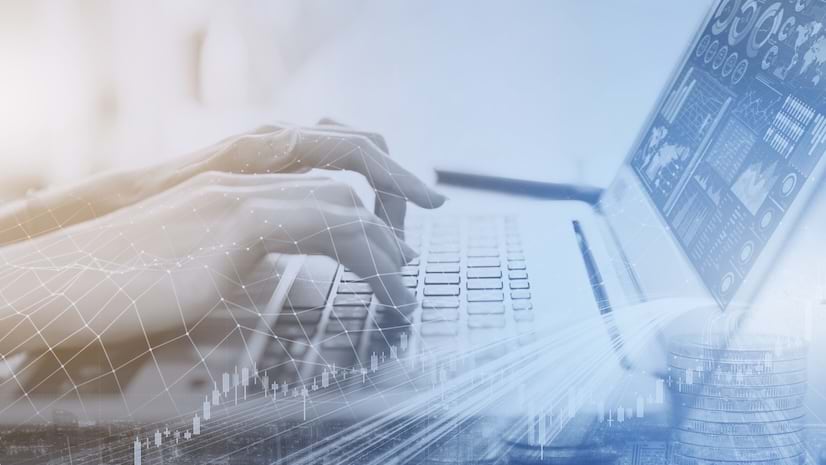 Hands typing on a keyboard with the monitor showing graphs and data