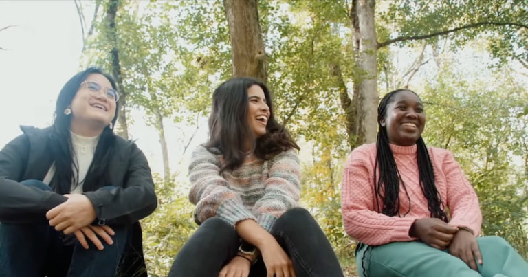 Three smiling young women sitting outdoors and talking