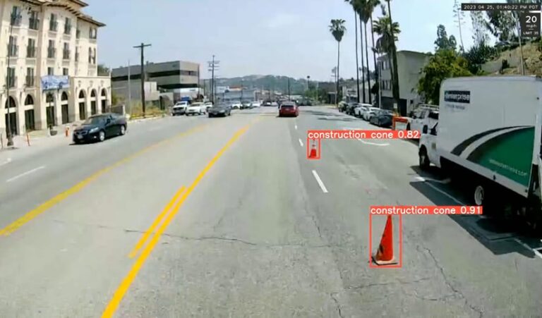 Photo of a street with palm trees and mountains in the distance. Two construction cones in between lanes are surrounded by labeled orange boxes.
