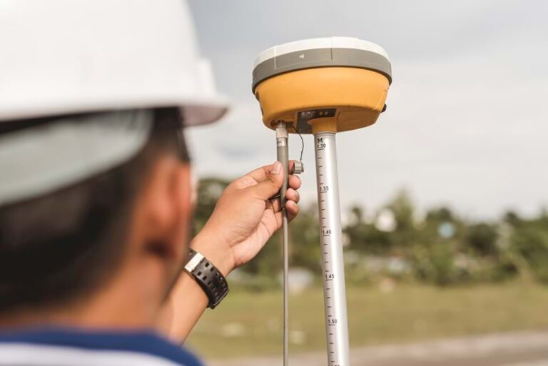 Photo of a man from behind his head depicting him adjusting a GNSS receiver against an out-of-focus background.