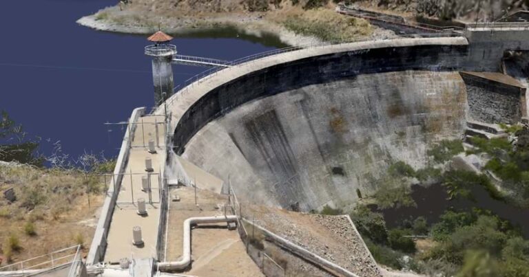 Three dimensional model of a dam, with a red-roofed tower and a body of water in the background.