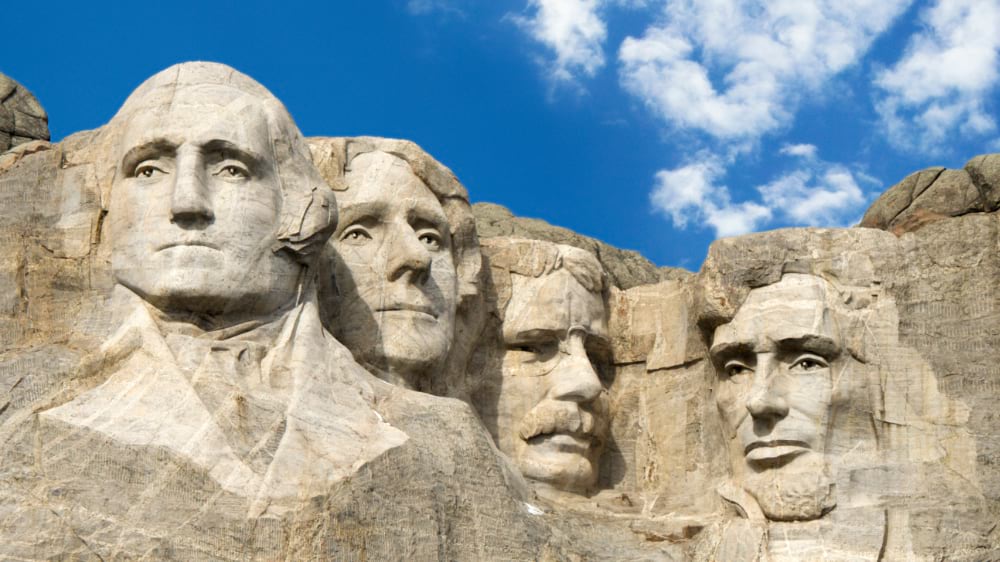 Mount Rushmore sculpture showing Washington, Jefferson, Roosevelt, and Lincoln against a blue sky.