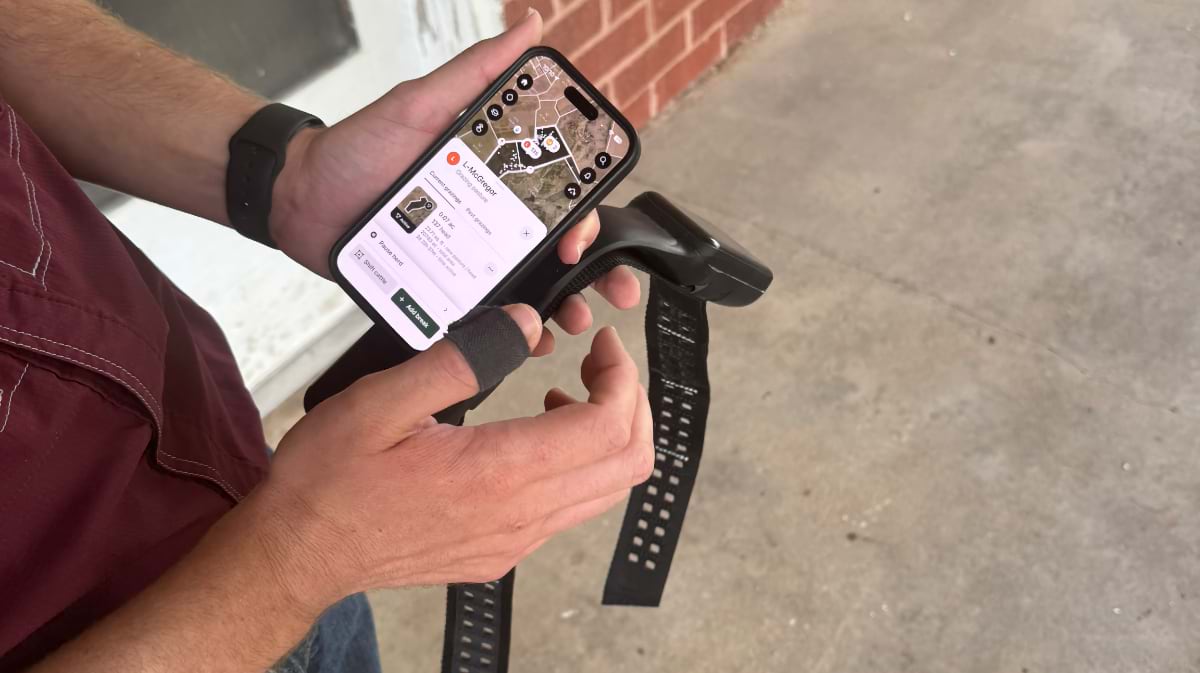 Hands holding a virtual fence collar and a smartphone displaying a pasture map of the McGregor Research Center.