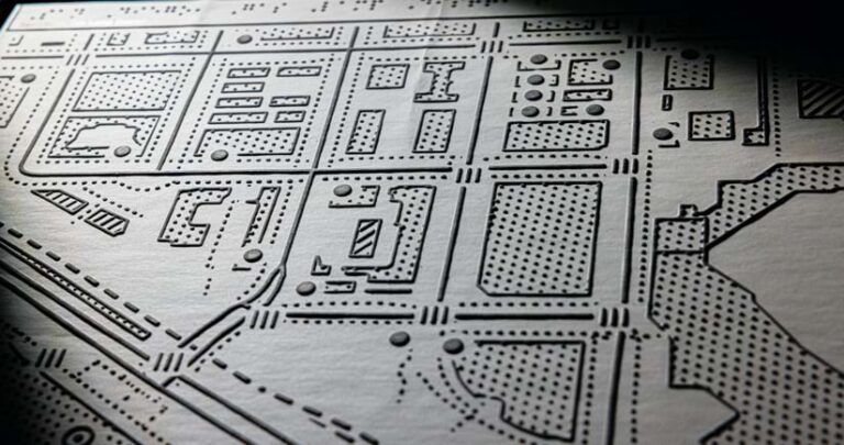 A black and white map with raised thick lines and shapes filled by raised dots is photographed at an angle to show features in relief.