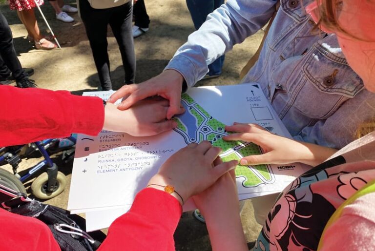 Three people gather around a physical paper map with raised features, touching the map with their hands.