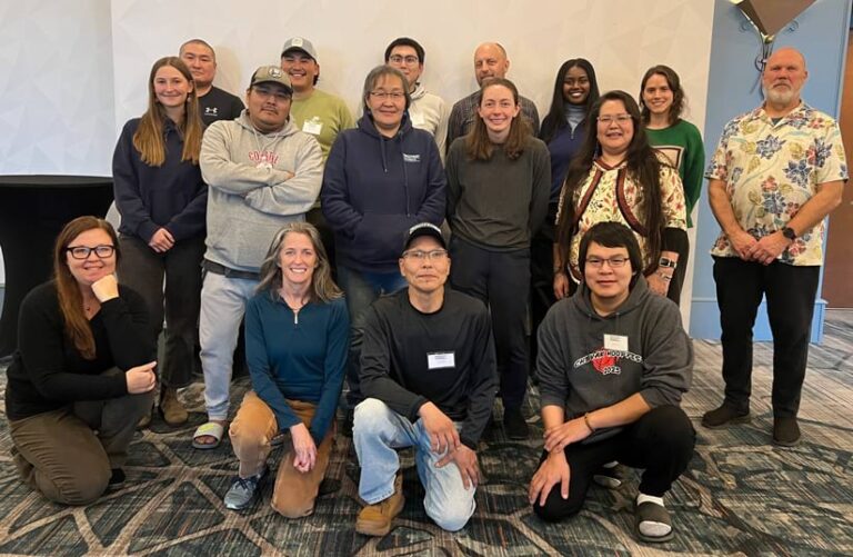 Group photo of people of various ages against a white and blue wall, with the front row of participants kneeling.