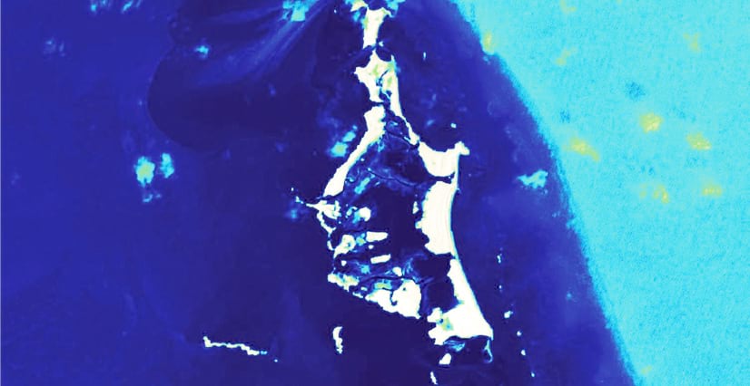A color-coded satellite image of a that same tropical island, showing the land in bright white, with water—including the ocean and inland water—shown in dark blue and light cyan.