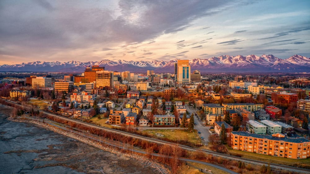 Aerial view of downtown Anchorage skyline at sunset with mountains behind.