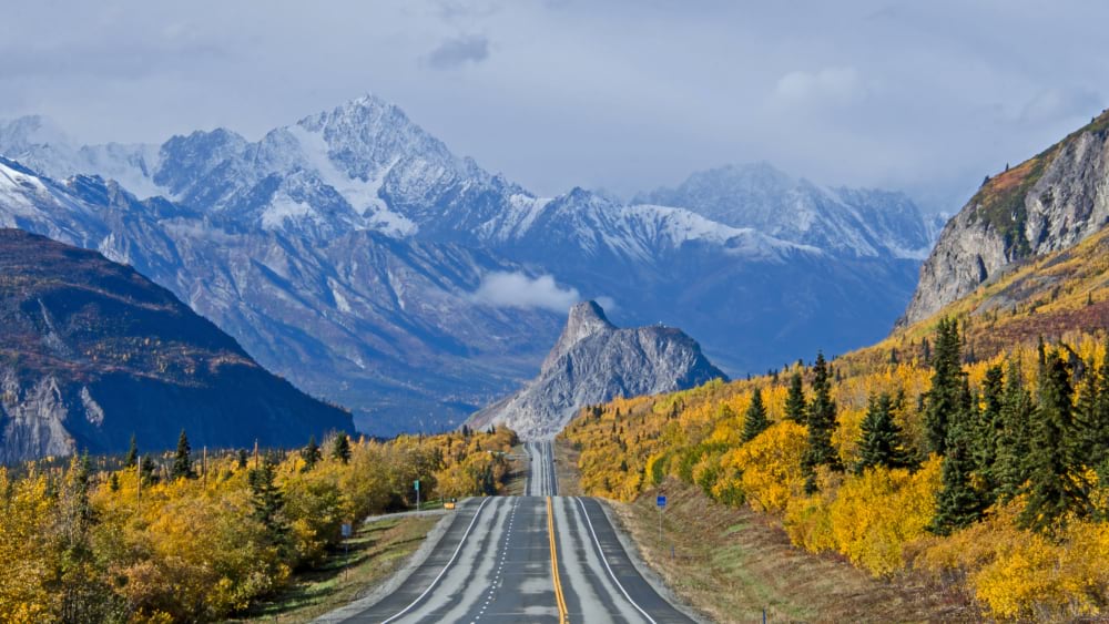 Two-lane highway leading toward snow-capped peaks along Alaska's Glenn Highway.