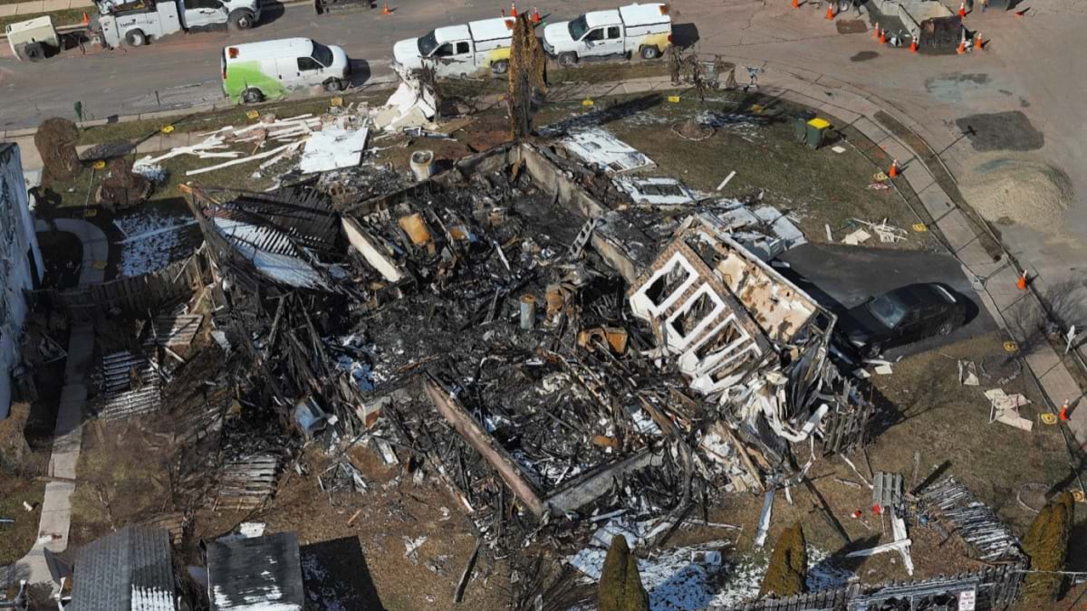 Aerial view of a burned-out home reduced to charred debris, surrounded by emergency vehicles.