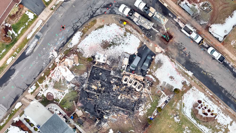 Overhead drone photo of a burned home's charred foundation amid debris on a snow-dusted street.